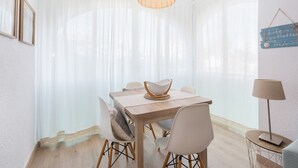 Un comedor con una mesa de madera, sillas blancas, una lámpara colgante de fibras tejidas y un letrero en la pared.