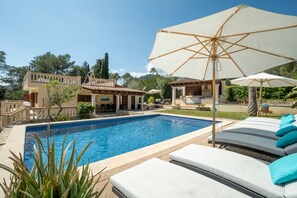 Une piscine entourée de chaises longues et de parasols, elle-même bordée d’un jardin aménagé et d’un bâtiment à deux étages.
