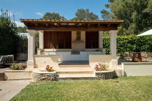 Cocina exterior con pérgola, armarios empotrados y encimera de piedra.