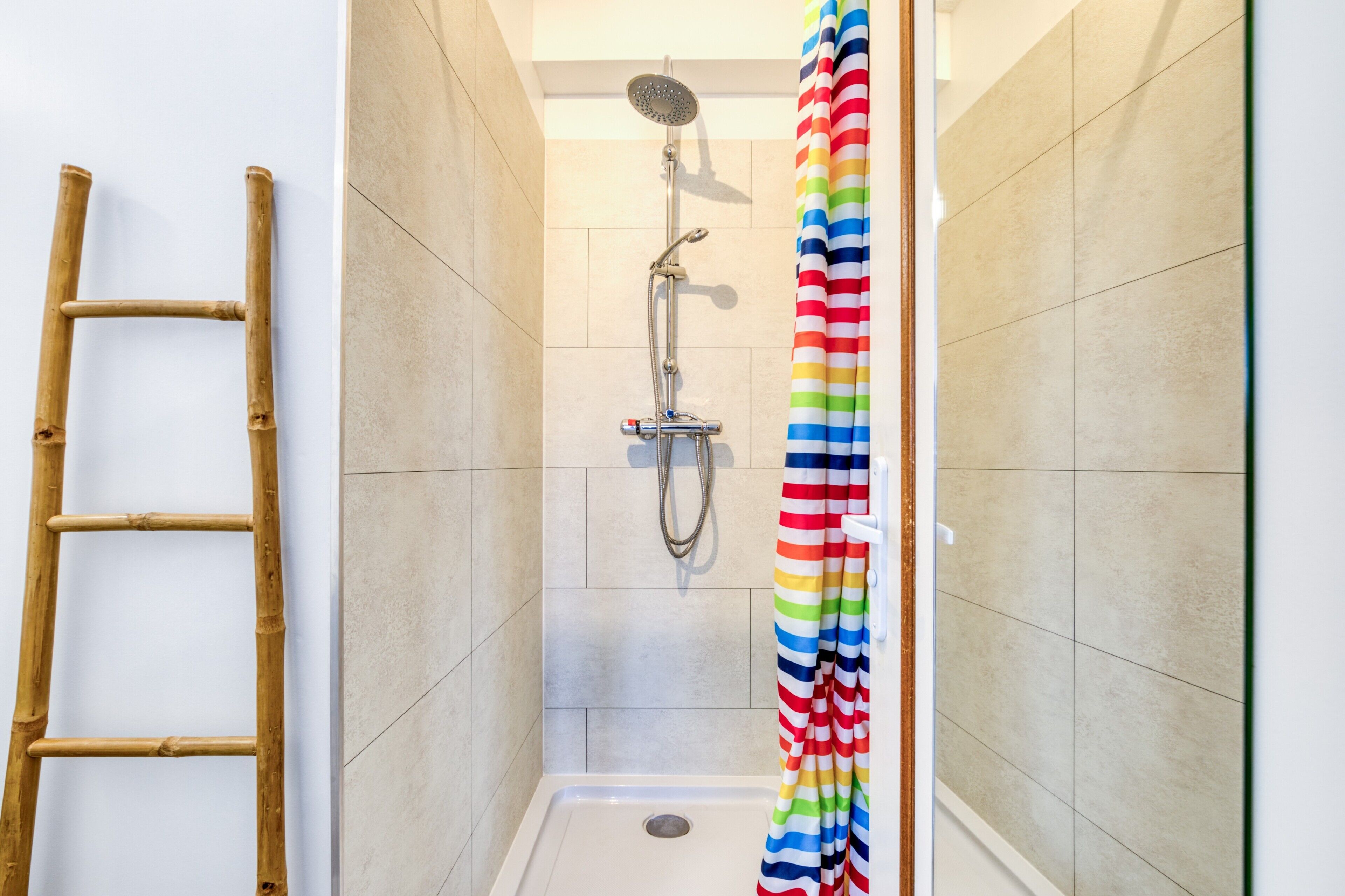 A shower with a rain showerhead, a colorful striped shower curtain, and a wooden ladder against the wall.