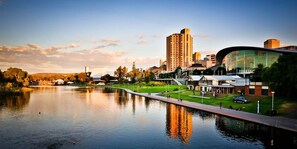 A waterfront cityscape with modern buildings, a curved glass structure, and a calm river.