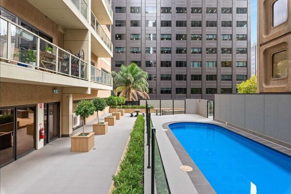 A modern building with a rooftop pool, outdoor seating, and a palm tree.