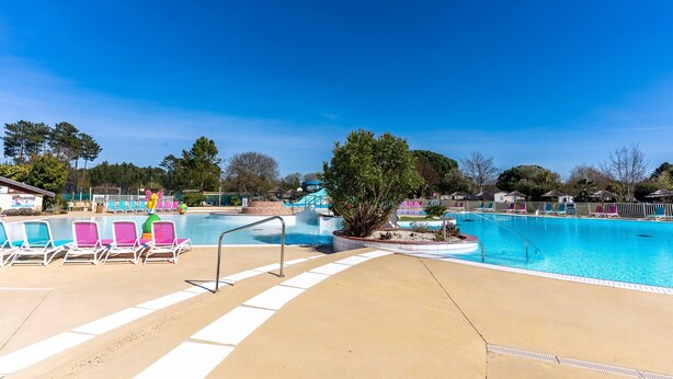 A swimming pool with lounge chairs, a small bridge, and a tree.