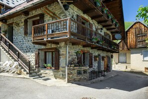 Un bâtiment en pierre doté d’un balcon en bois, d’un escalier et d’un petit espace porche agrémenté de plantes en pot.
