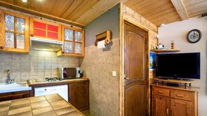 Una cocina con armarios de madera, estufa, microondas y televisor.