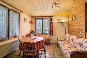 A cozy room with a wooden ceiling, a round dining table with chairs, a sofa, and a window with curtains.