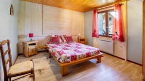 Een slaapkamer met houten lambrisering, een bed, nachtkastjes, een stoel en een raam met gordijnen.