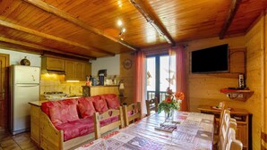 Een gezellig chaletinterieur met een houten plafond, een eettafel met een sprei, een bank en een keukenhoek.