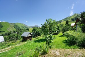 A rural landscape with a small wooden cabin, lush greenery, and distant mountains.