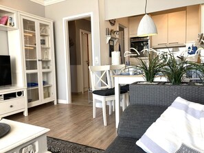 Una sala de estar moderna con un sofá gris, una mesa de comedor blanca y una cocina con un armario blanco y un horno.