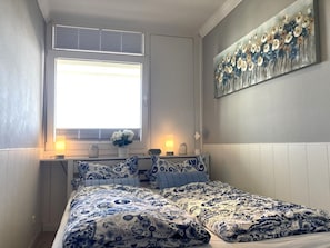 Un dormitorio con una cama, una ventana, un cuadro y lámparas de noche.