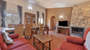 Una sala de estar con chimenea de piedra, sofás rojos, un comedor con sillas de mimbre y un televisor.