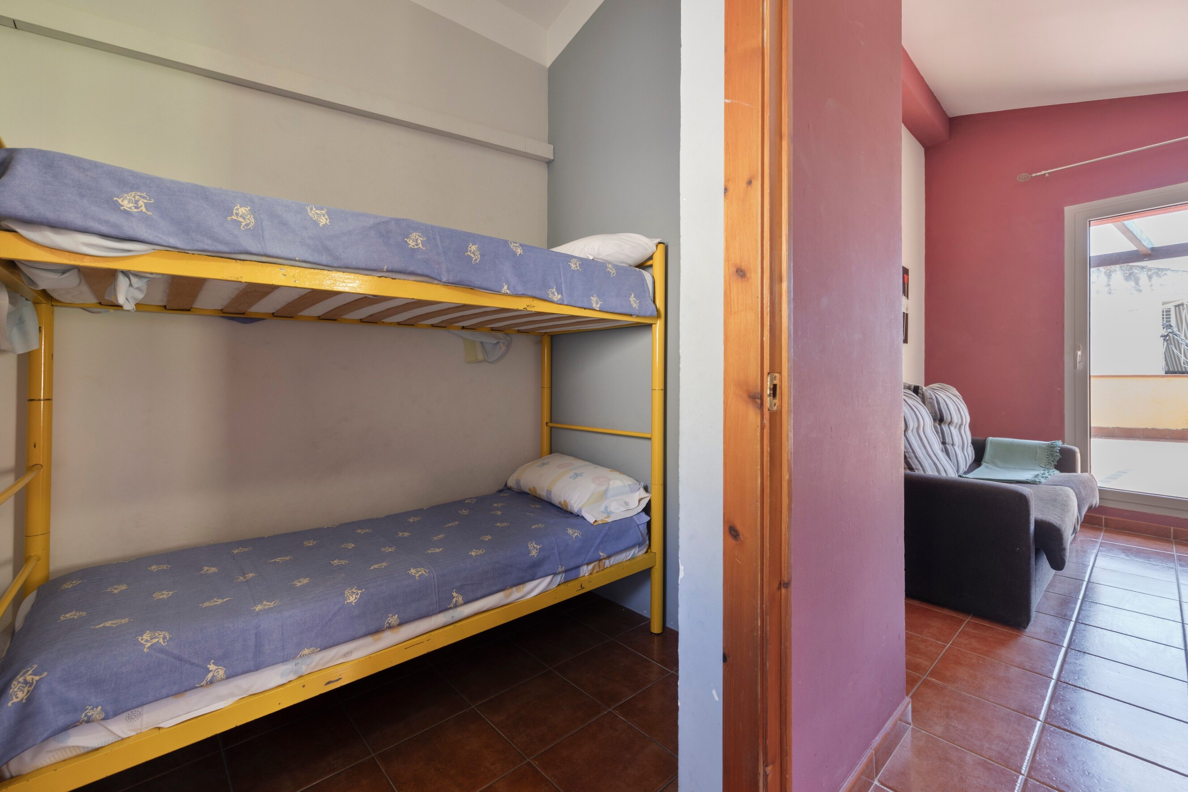 A bunk bed room with a window, a sofa, and a door.