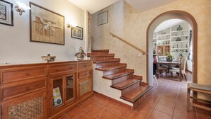 Una escalera conduce a un comedor con piso de baldosas, armarios de madera y obras de arte colgadas en la pared.