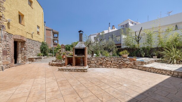Un patio con zona de barbacoa de piedra, un muro de piedra y un edificio con fachada amarilla.