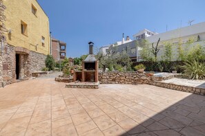 Une cour avec un espace barbecue en pierre, un mur en pierre et un bâtiment à la façade jaune.