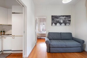 Ein modernes Wohnzimmer mit einem grauen Sofa, eine Küche mit weißen Schränken und ein Schwarz-Weiß-Stadtbild an der Wand.