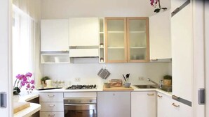 Una cocina moderna con armarios blancos, horno empotrado, estufa a gas y pileta de acero inoxidable.