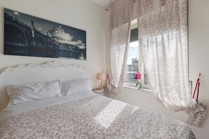 Ein Hotelzimmer mit einem großen Bett, einem Gemälde mit Nachtansicht, floralen Vorhängen und Blick auf die Stadt durch das Fenster.
