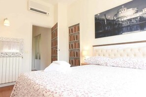 Une chambre d’hôtel avec un lit, une grande bibliothèque, un radiateur et un tableau représentant un château.