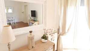 Una habitación con un espejo grande, un aparador de madera, una lámpara, una orquídea en maceta y un televisor sobre un mueble.