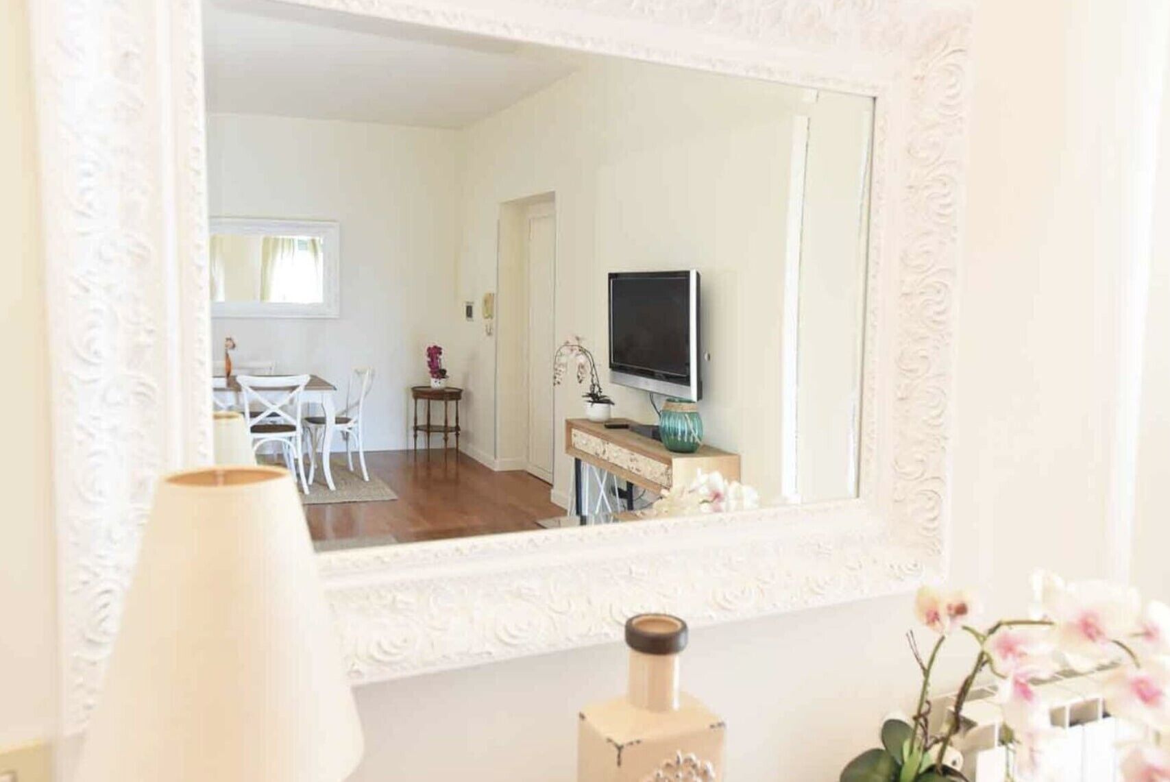 Una habitació amb un mirall gran, una televisió, una taula petita amb un ram i una cadira.