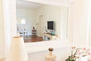 Une pièce avec un grand miroir, une télévision, une petite table avec un vase et une chaise.