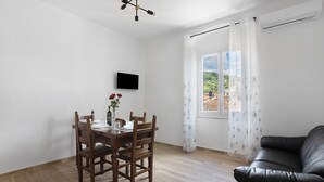Una habitación con una mesa de comedor, sillas, un sofá de cuero negro, un televisor de pantalla plana y una ventana con cortinas.