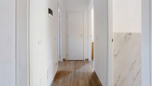 Un pasillo con suelo de madera, paredes blancas y una puerta al final.