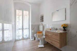 A modern bathroom with a toilet, bidet, wooden vanity, and a large mirror.