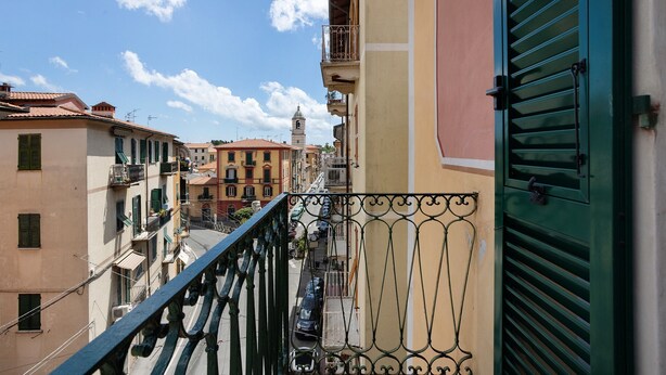 Un balcón con barandilla de metal que da a una calle con edificios y una torre a lo lejos.