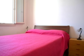 Un dormitorio con una cama, una mesita de noche, una lámpara y una ventana.
