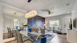 A modern dining area with a glass table, blue chairs, and a cityscape mural on the wall.
