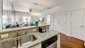 A modern kitchen with granite countertops, a double sink, a built-in dishwasher, and a large mirror.