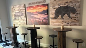 Een rij ronde tafels met krukken, elk met een kaars erop, voor een muur met drie houten decoraties.