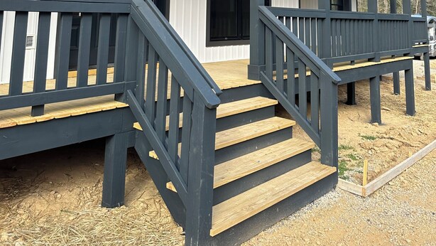 Een gebouw met twee verdiepingen, een overdekte veranda, houten trappen en zwarte leuningen.