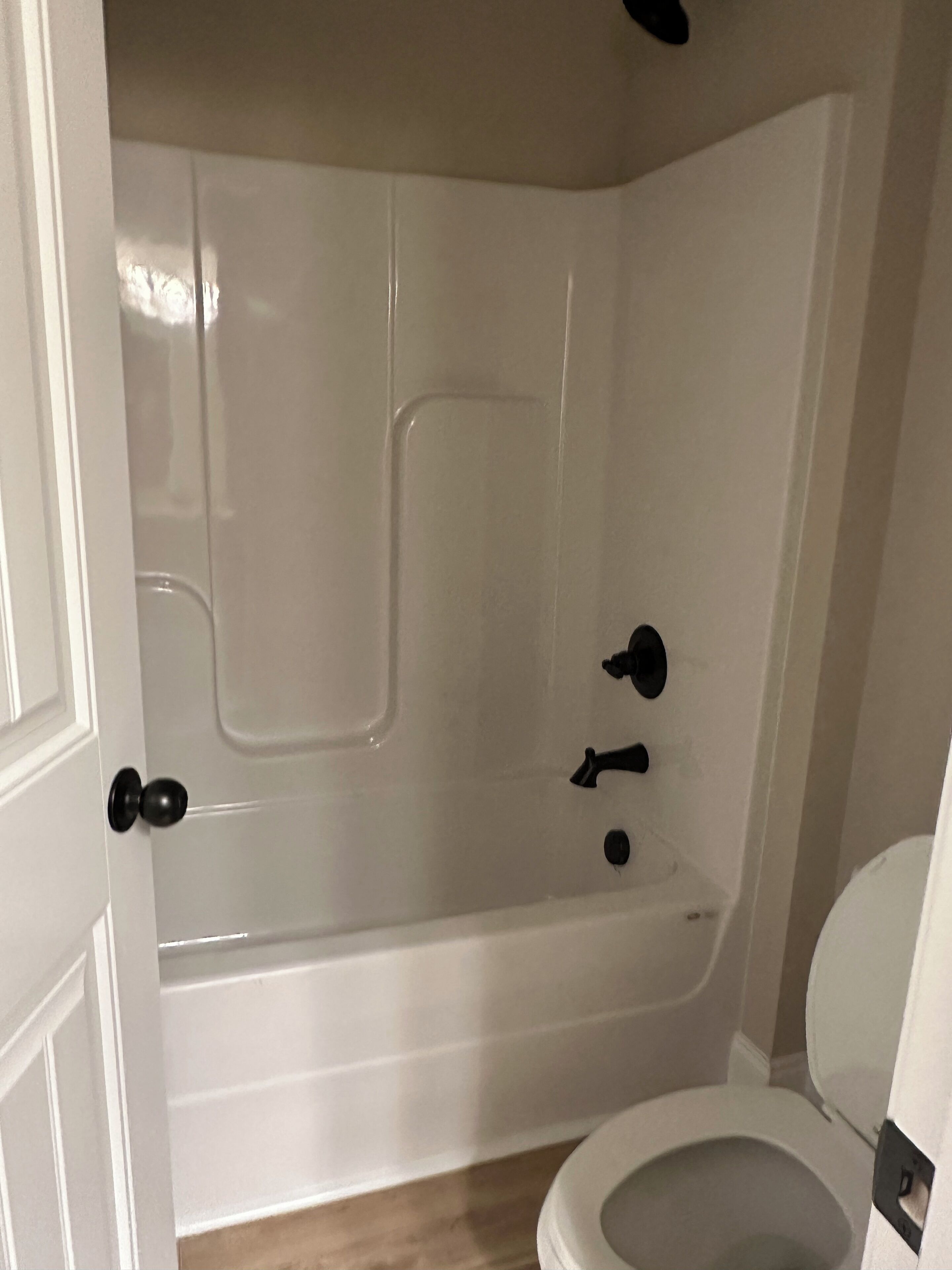A bathroom with a white bathtub, a toilet, and a door.