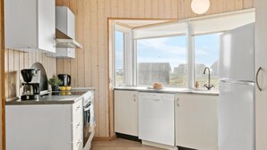 Cozinha moderna com armários brancos, cafeteira, chaleira e janela com vista para edifícios.