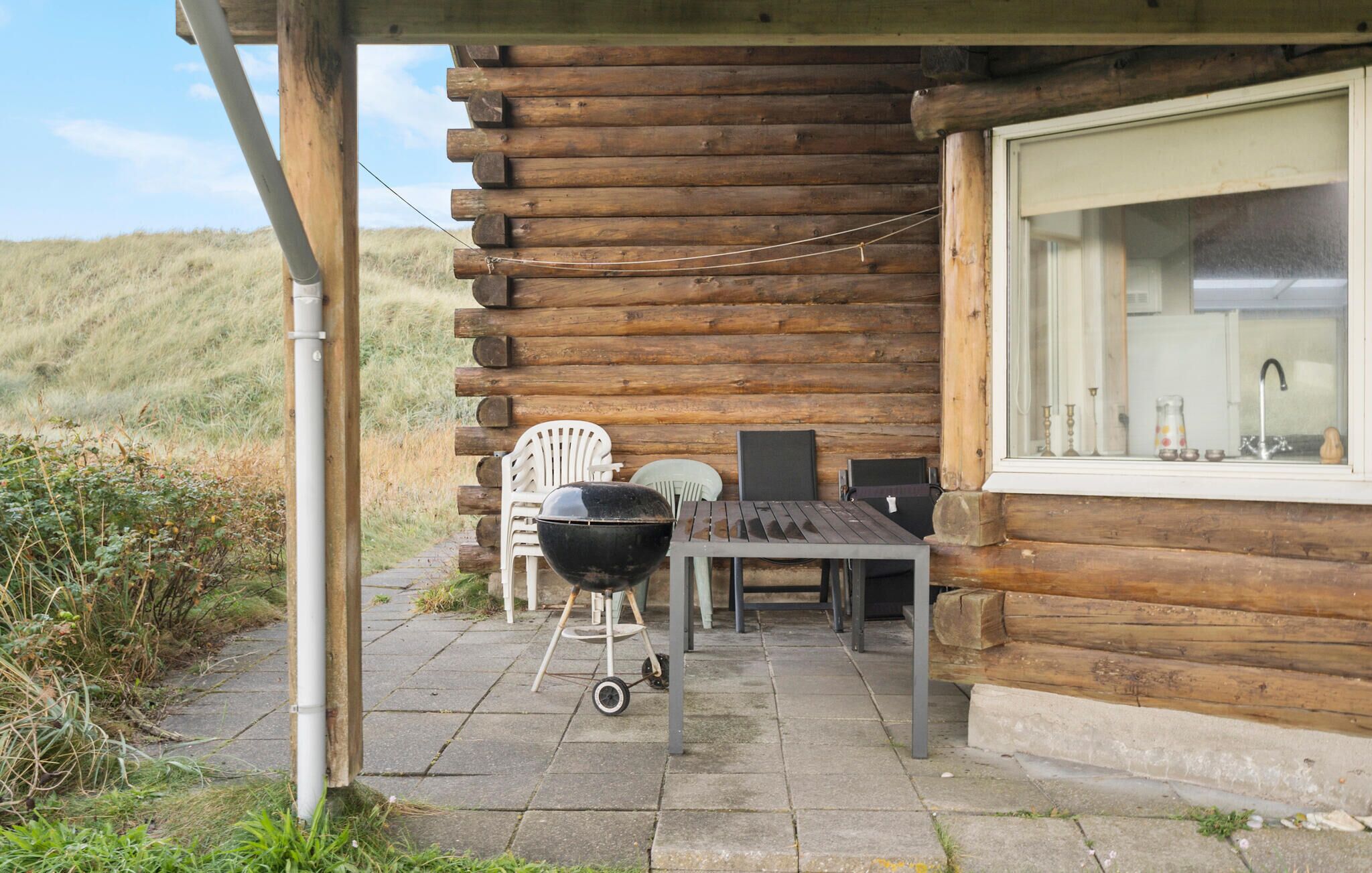Een blokhut met een patio, inclusief een barbecue, stoelen en een tafel.