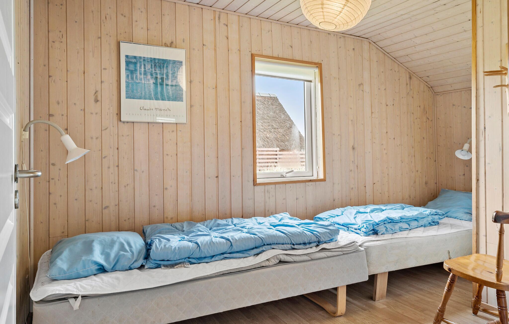 Quarto pequeno com cama de solteiro, paredes de madeira e janela.