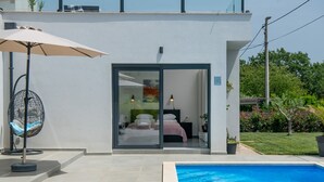 Une maison moderne dotée d’une piscine, d’une entrée avec une porte en verre et d’un ventilateur à l’extérieur.