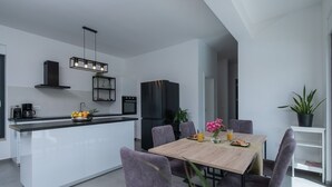 Une cuisine moderne dotée d’un îlot central, d’appareils électroménagers noirs et d’un coin repas avec une table en bois et des chaises violettes.