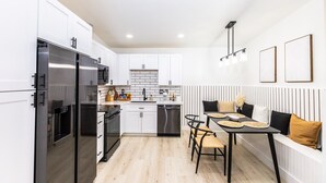 Uma cozinha moderna com armários brancos, uma geladeira preta e uma área de refeições com uma mesa e cadeiras pretas.