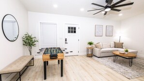 Uma sala de estar moderna com mesa de futebol, sofá, mesa de centro, um banco e ventilador de teto.