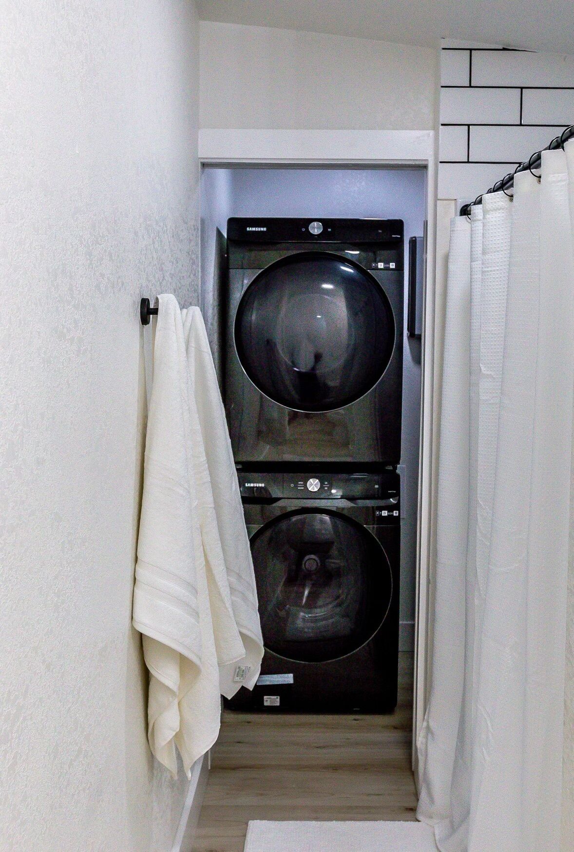 Une buanderie équipée de deux machines à laver superposées, d’un porte-serviettes et d’un rideau de douche.