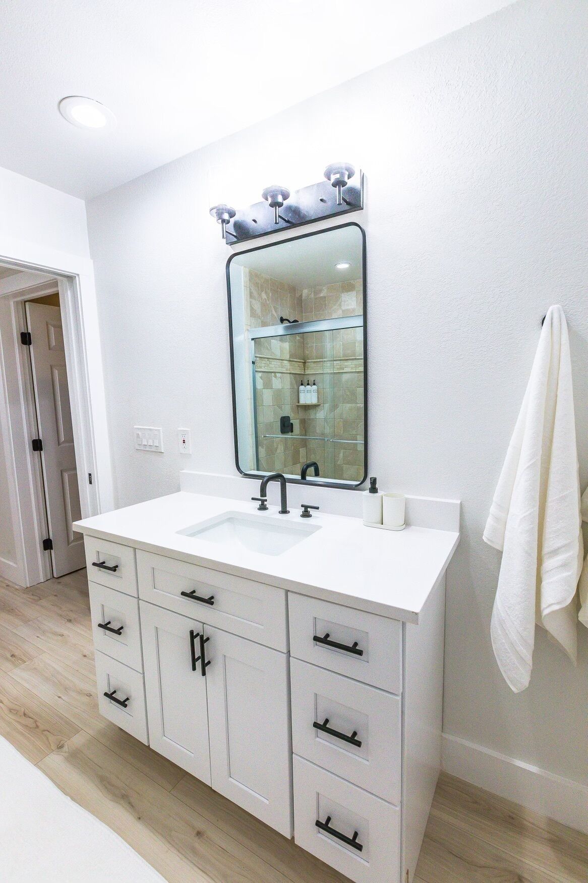 A modern bathroom with a white vanity, a large mirror, and a glass shower enclosure.