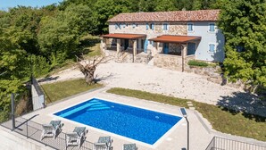 Une villa en pierre dotée d’une piscine, entourée d’arbres et baignée par un ciel dégagé.