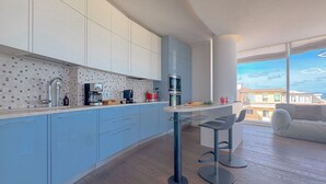 Een moderne keuken met lichtblauwe kastjes, een witte werkblad en een eethoek met twee barkrukken.