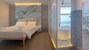 Een moderne hotelkamer met een bed, een groot muurschildering, een badkuip en uitzicht op zee.