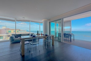 A modern dining area with a view of the sea, a large window, and a high ceiling.